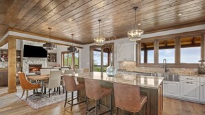 A spacious kitchen with a large island, wooden ceiling, and a stone backsplash.