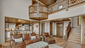 A spacious living area with a high ceiling, a dining table, leather sofas, and a staircase leading to an upper level.