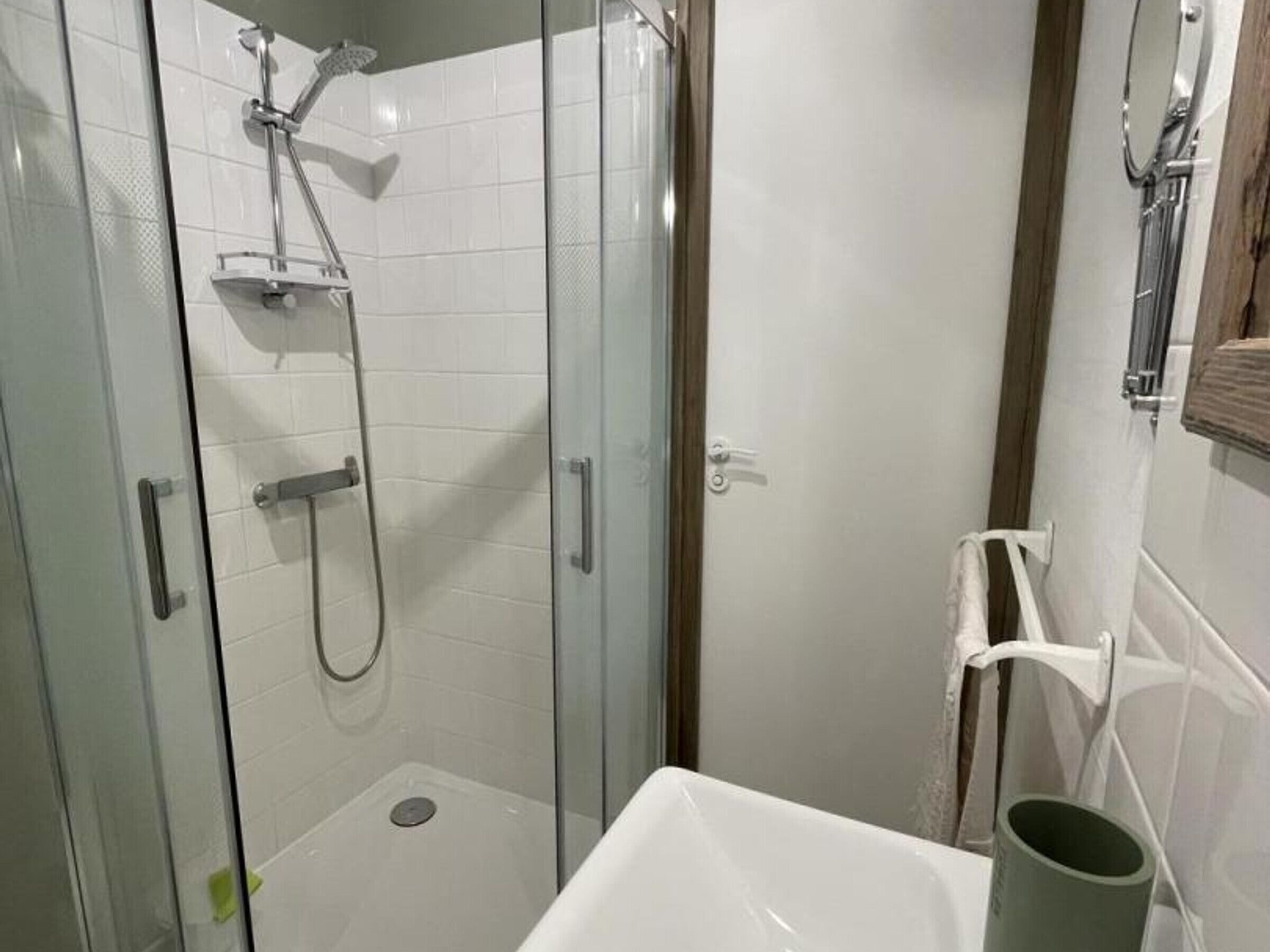 A glass-enclosed shower with a handheld showerhead and a wall-mounted faucet.