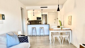 Una sala moderna con un sofá a rayas, una mesa de comedor con sillas blancas y una cocina al fondo.