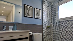 Un baño con inodoro, lavabo y ducha. Hay dos cuadros en la pared.