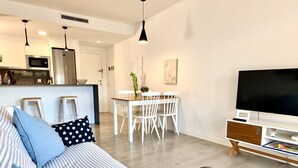 Una sala de estar moderna con un sofá a rayas, un televisor de pantalla plana y una zona de comedor con una mesa y sillas blancas.