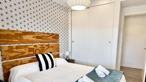 Una cama bien hecha con sábanas blancas y una almohada a rayas, una manta azul y toallas enrolladas sobre la cama.