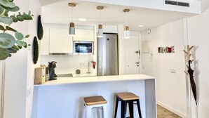 A modern kitchen with white cabinets, a stainless steel refrigerator, a microwave, and pendant lights. There are two stools at the counter.