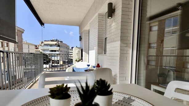 A balcony with a white table, potted plants, and a view of buildings.