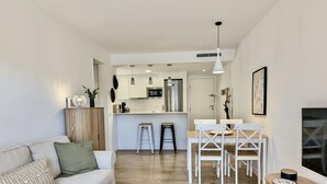A modern living room with a sofa, a dining area with a table and chairs, and a kitchen in the background.