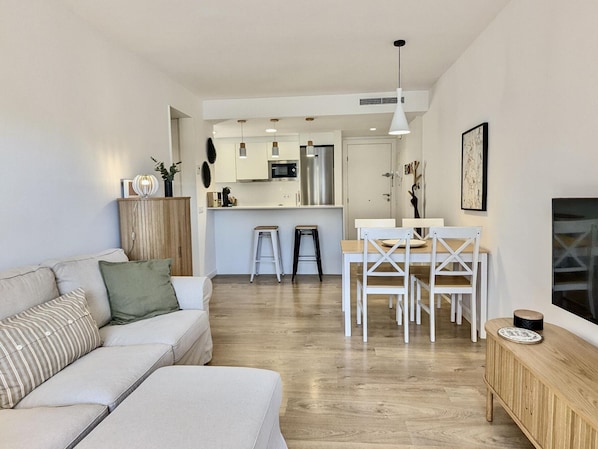 A modern living room with a sofa, a dining area with a table and chairs, and a kitchen in the background.