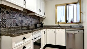 A kitchen with white cabinets, a patterned backsplash, a Bosch dishwasher, and a window with blinds.