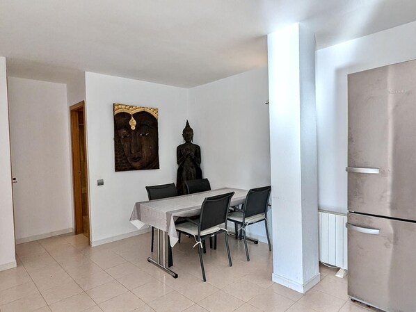 Un comedor con una mesa, sillas, una estatua de Buda y un refrigerador.