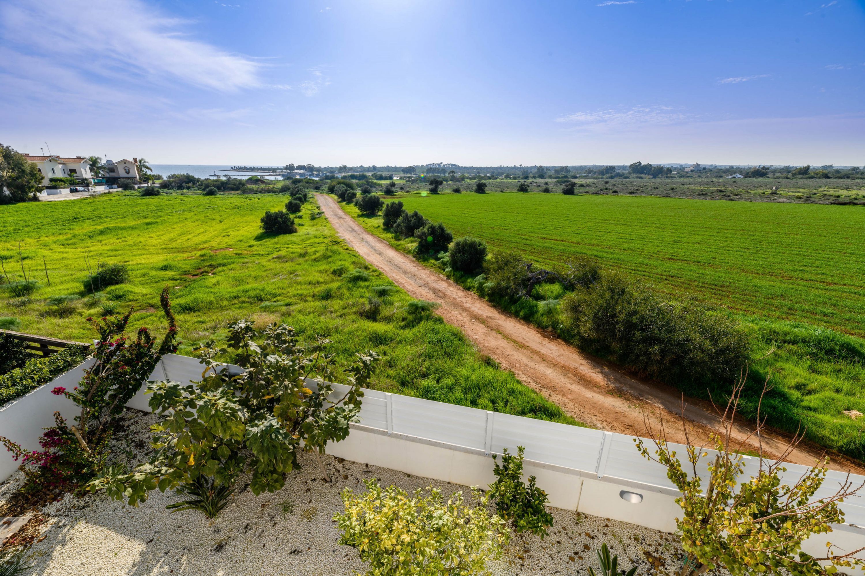 A rural landscape with a dirt road leading through green fields and a white building in the distance.