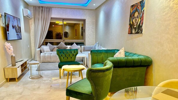 A modern living room with a green sofa set, a glass coffee table, and a beige couch.