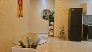 A modern living room with a glass table, a black refrigerator, and a painting on the wall.