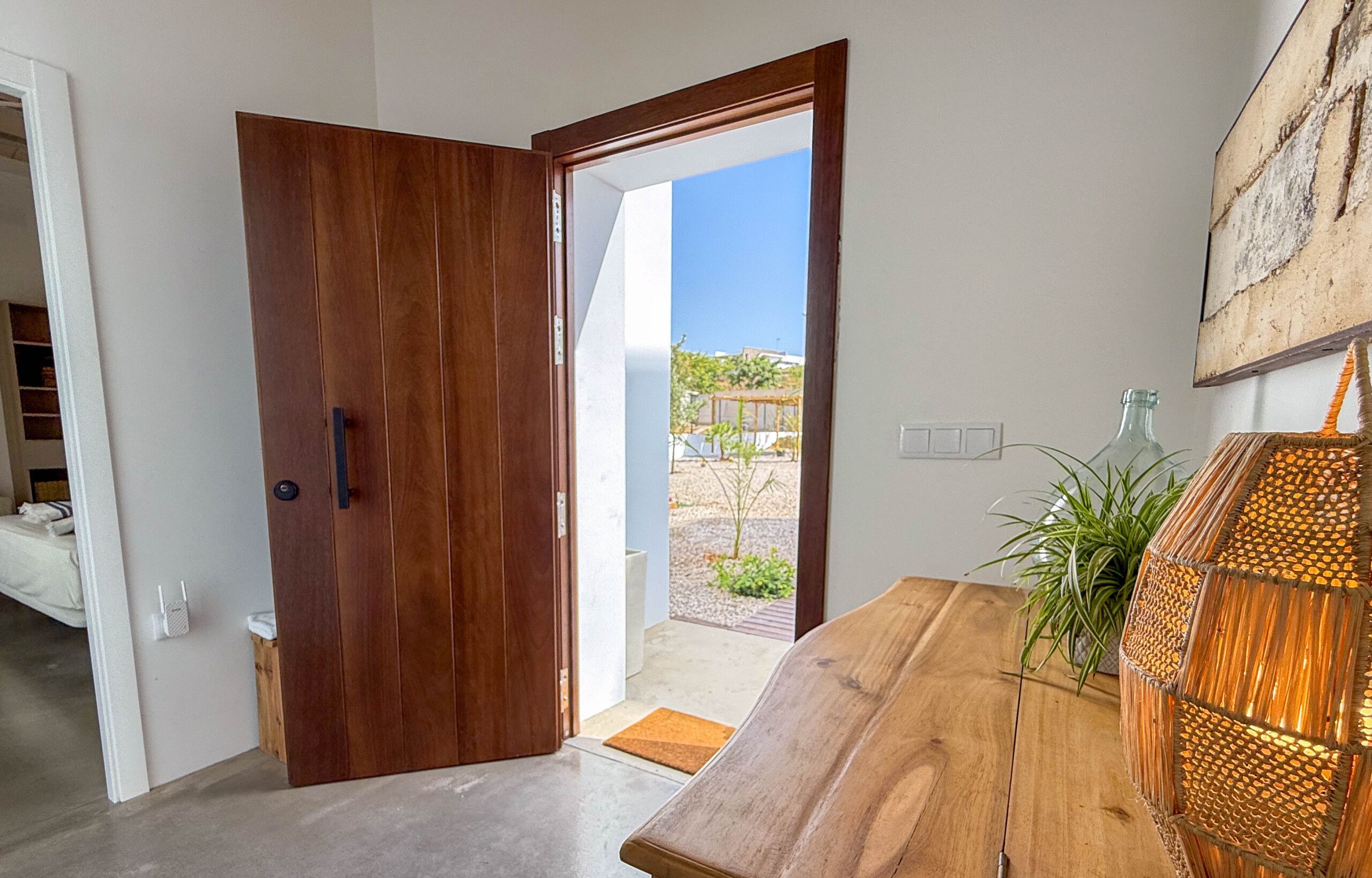 A wooden door leading to a balcony with a view of a garden and buildings.