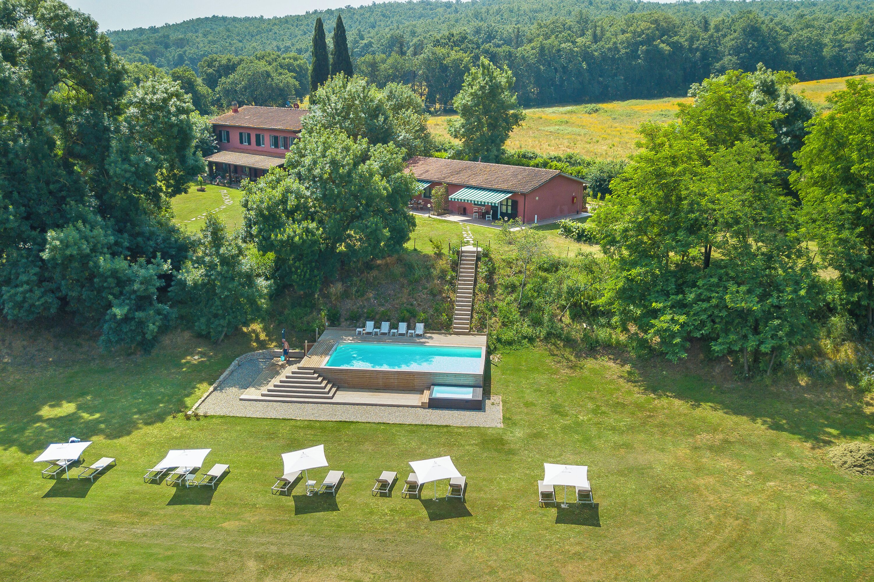 A large swimming pool surrounded by lounge chairs, with a house and a red building in the background.