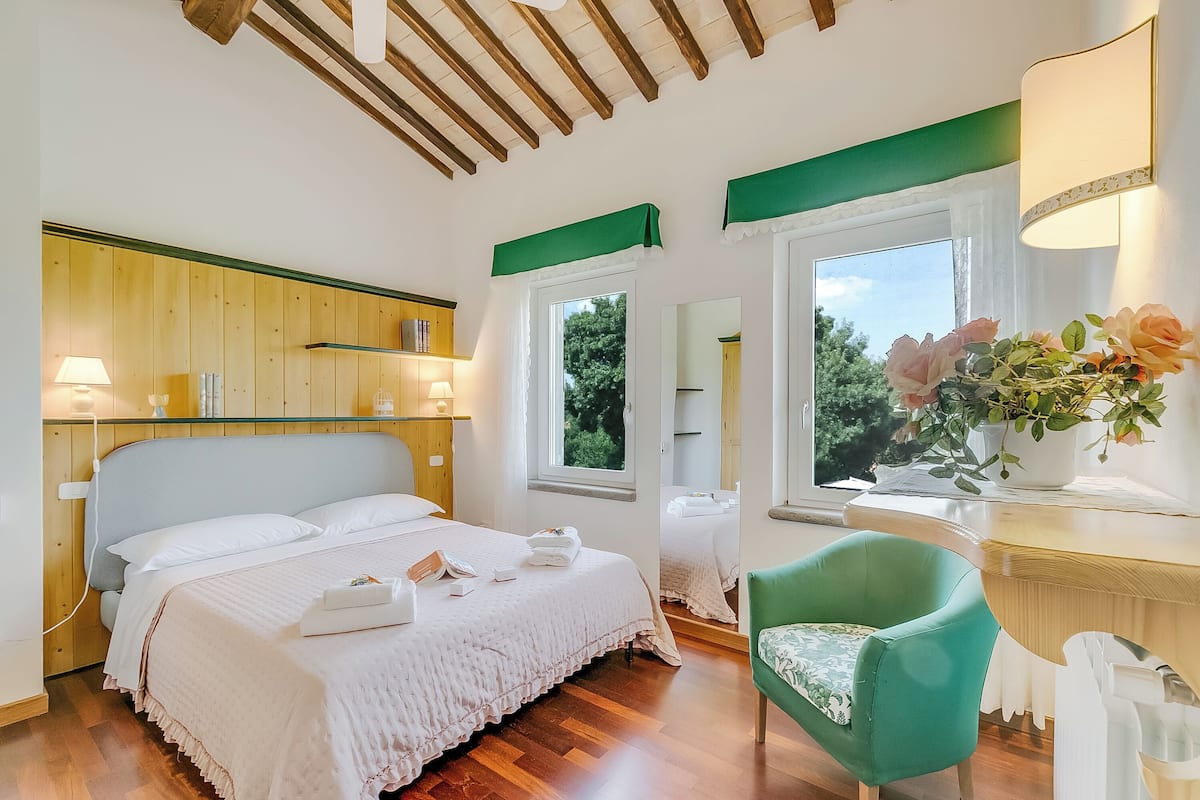 A bedroom with a wooden headboard, a large bed with white linens, a green armchair, and a bedside table with a lamp.