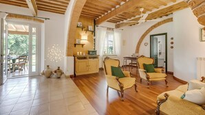 Een ruime woonkamer met houten vloeren, een hoog plafond met zichtbare balken en een gezellige zithoek met twee fauteuils en een bank.
