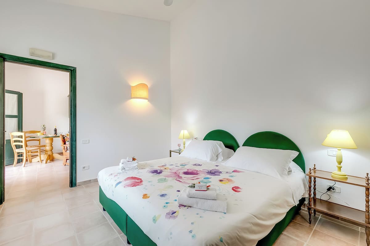 A neatly made bed with a floral bedspread, a green headboard, and two bedside lamps.