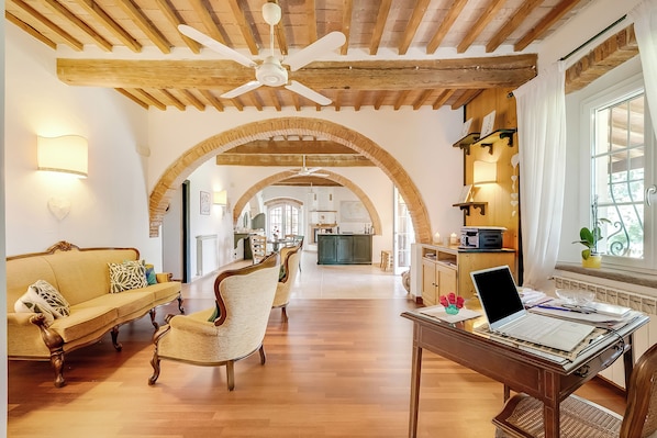 A spacious living area with a wooden ceiling, a sofa, a dining table with a laptop, and a kitchen in the background. - Relaxing Family Podere Delle Rose Pool & Garden (Civitella Paganico)