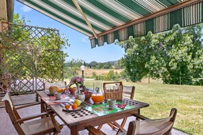 An outdoor dining area with a table set for two, surrounded by chairs, a wicker basket, and a view of a grassy landscape. - Relaxing Family Podere Delle Rose Pool & Garden (Civitella Paganico)