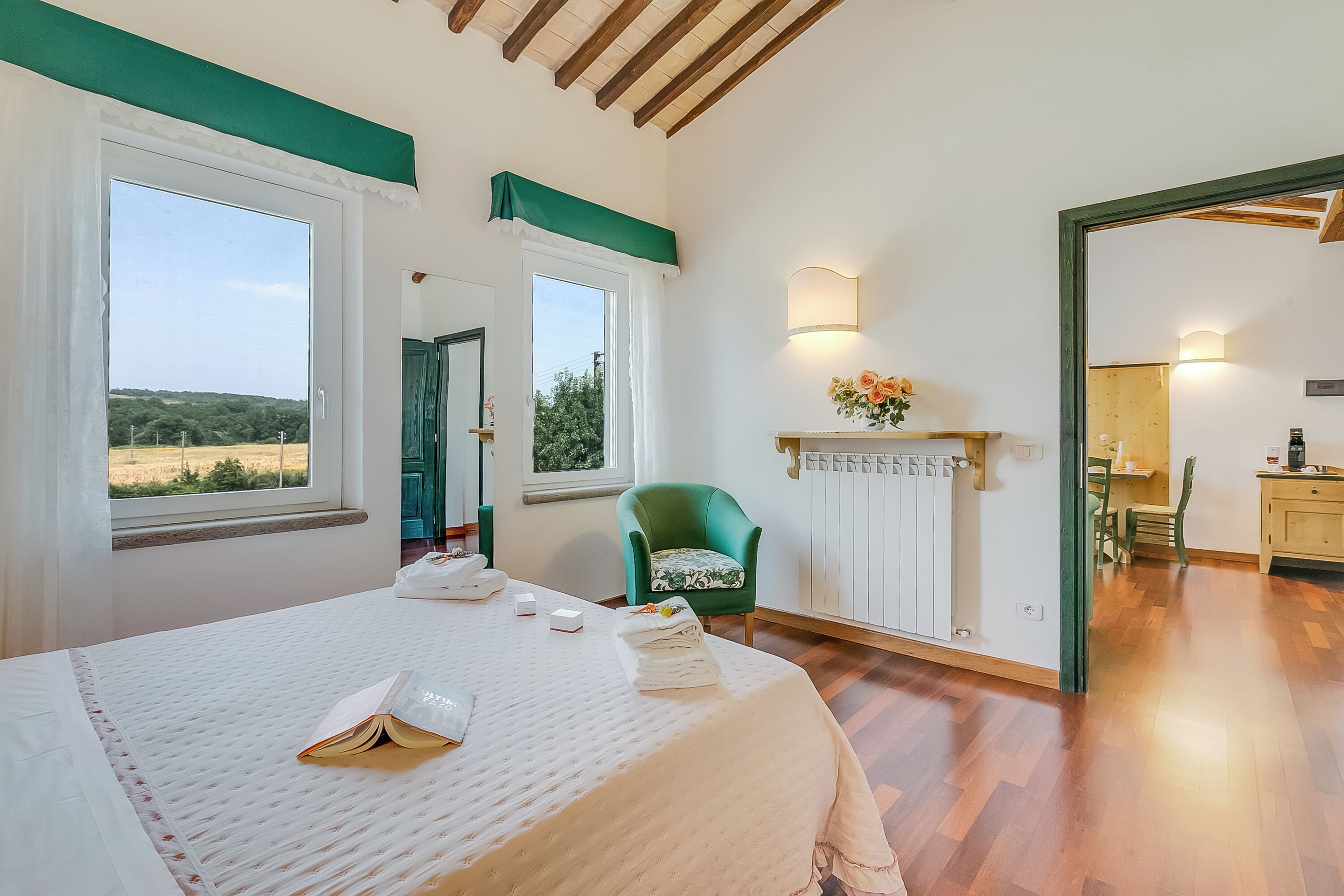 Quarto com cama, uma poltrona verde, radiador e vista para o exterior.