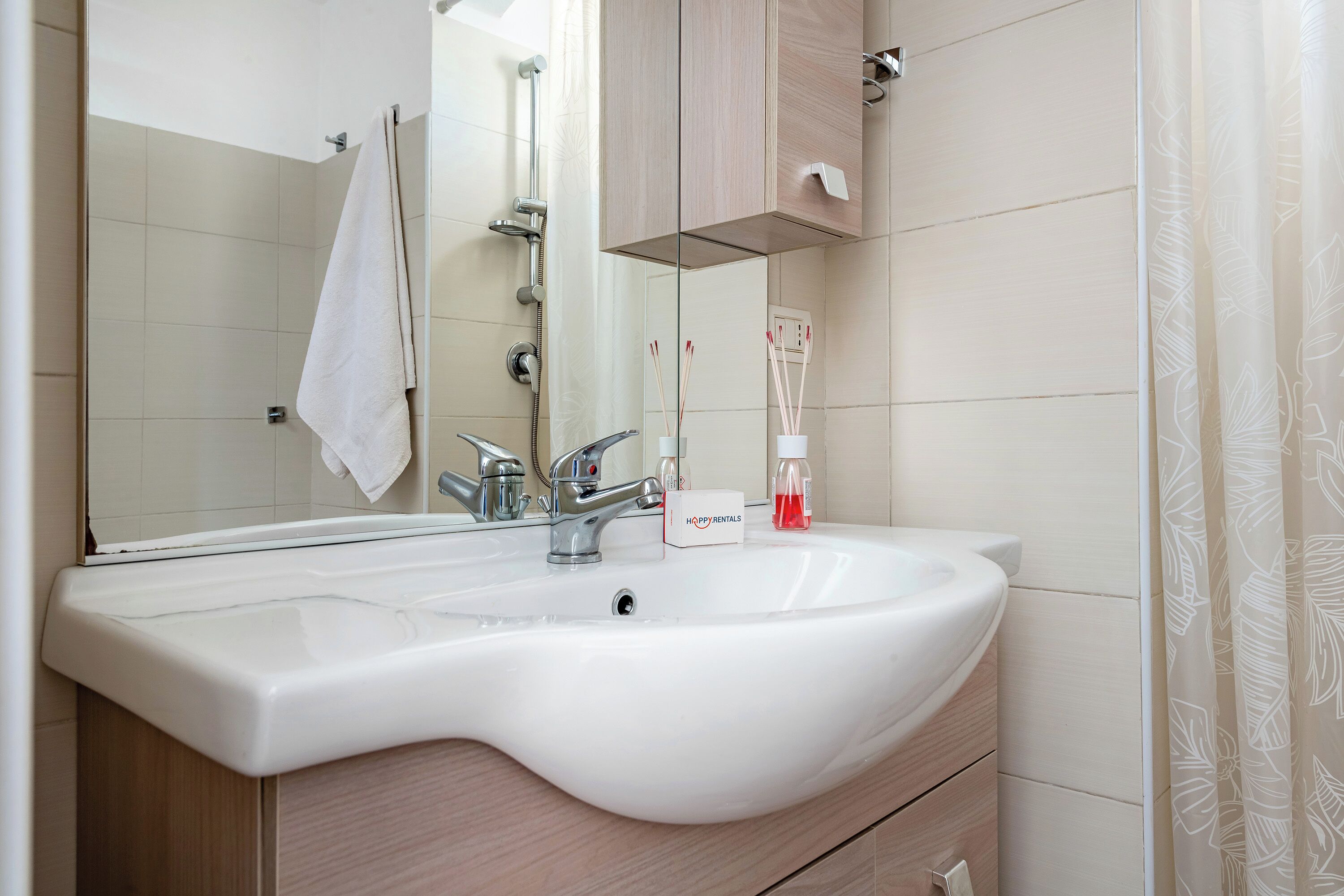 A bathroom with a white sink, a mirror, a towel hanging on the wall, and a shower area.