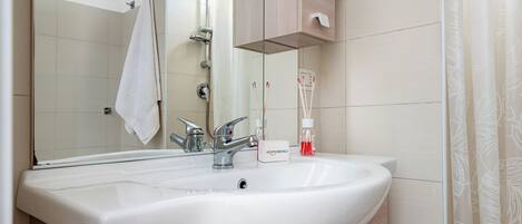 Ein Badezimmer mit einem weißen Waschbecken, einem Spiegel, einem Handtuch an der Wand und einer Duschkabine.
