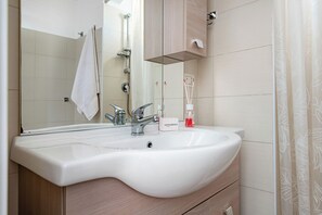 Ein Badezimmer mit einem weißen Waschbecken, einem Spiegel, einem Handtuch an der Wand und einer Duschkabine.