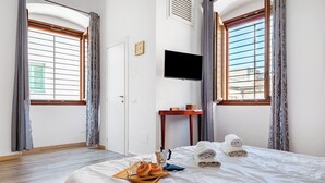 A hotel room with a bed, a flat-screen TV mounted on the wall, a small wooden table, and a window with curtains. - Giosue' Apartment Near Bari (Adelfia)