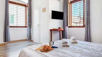 Quarto de hotel com cama, televisão de tela plana na parede, mesa de madeira e janela com cortinas.
