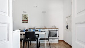 A small kitchen with a white table, black chairs, a stove, and a framed picture on the wall. - Giosue' Apartment Near Bari (Adelfia)