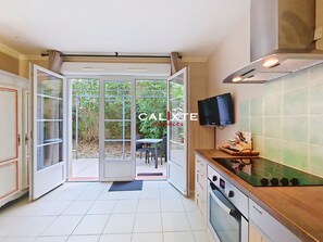 Eine Küche mit offener Tür zum Balkon, einem eingebauten Backofen und einem an der Wand montierten Fernseher.