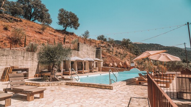 Un área de piscina con sillones de descanso, sombrillas y un deck de baldosas de piedra.