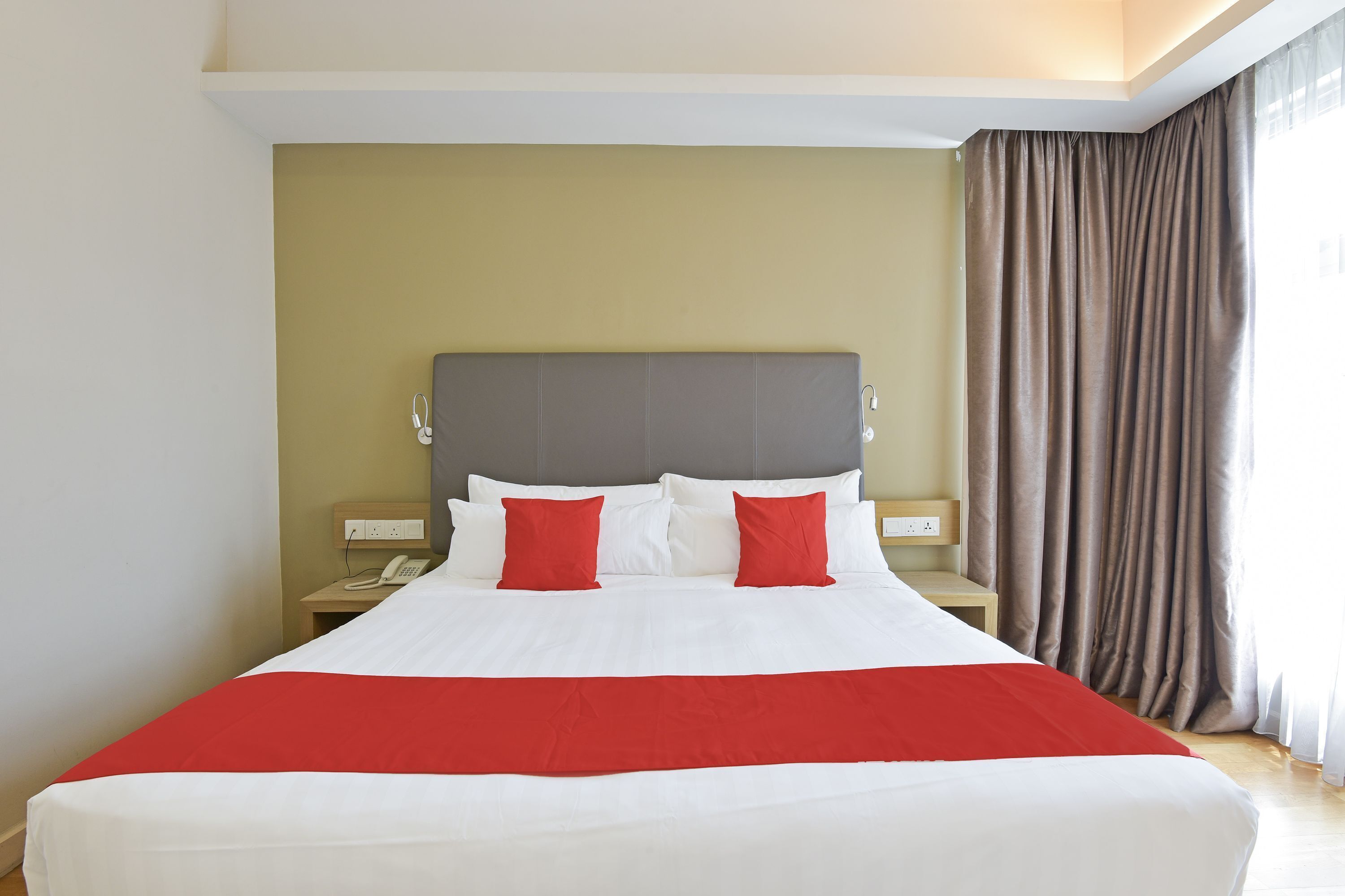 Habitación de hotel con una cama grande, cabecera, mesita de noche con teléfono y ventana con cortinas.