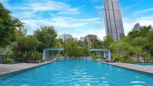 Una piscina con sillas de descanso y un pabellón, rodeada de árboles y edificios.