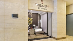 Zona de recepción con suelo de mármol, mostrador de recepción, candelabro y un cartel en la pared para Suasana Suites.