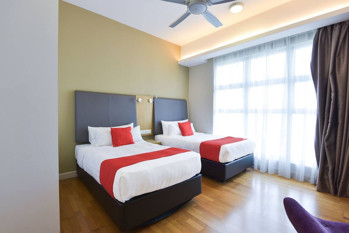 A hotel room with two beds, a ceiling fan, and large windows with curtains.