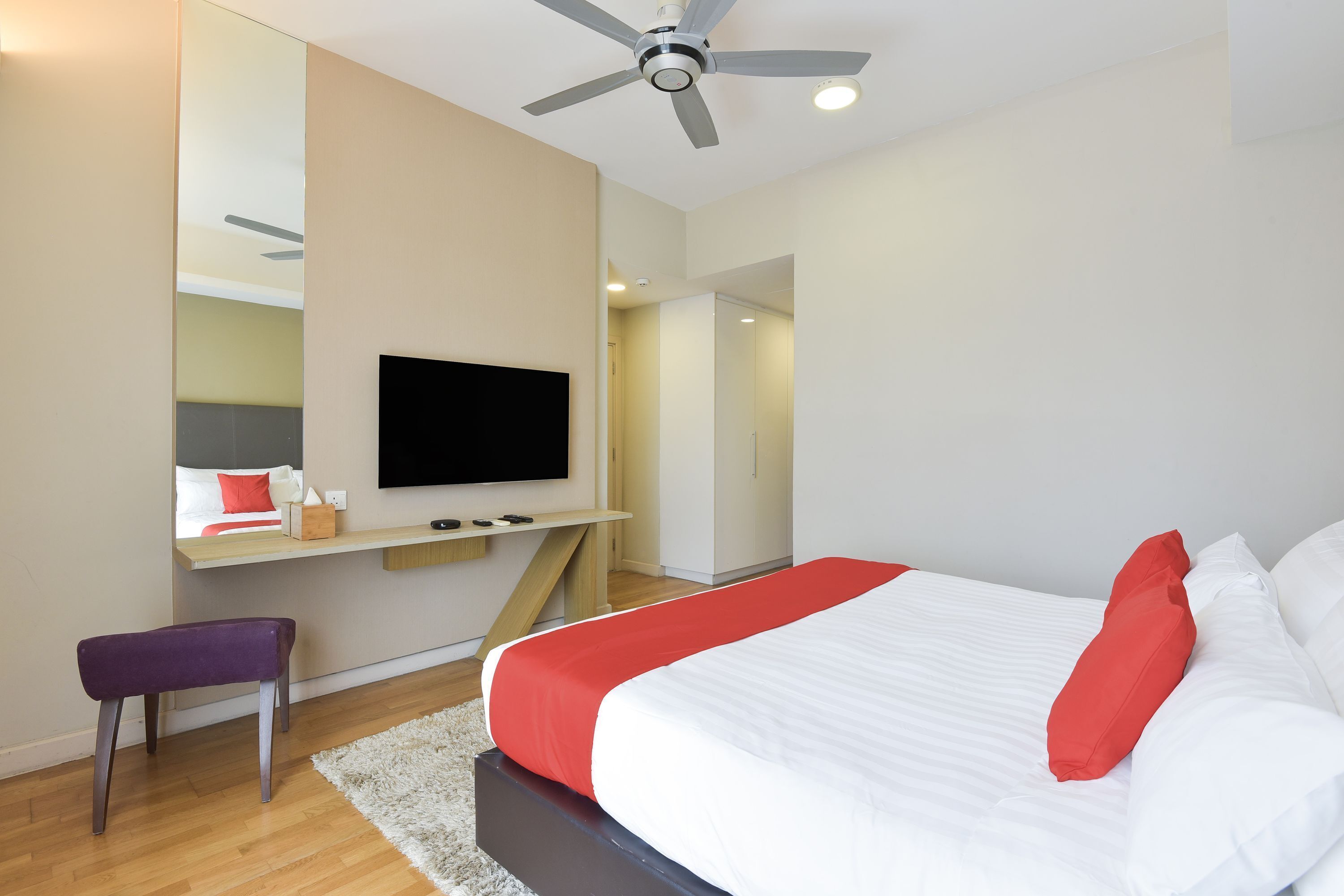 Quarto de hotel moderno com uma cama grande, televisão de tela plana na parede, ventilador de teto e um banco de madeira.