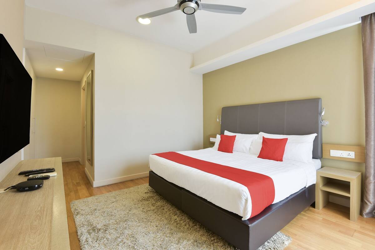 A bedroom with a bed, a ceiling fan, a TV, and a bedside table.