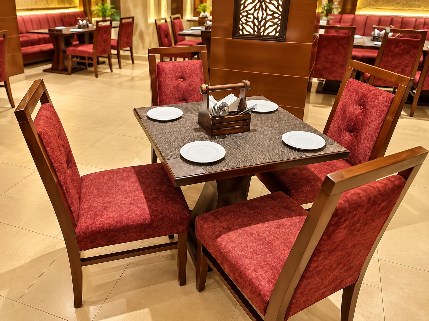 Comedor con una mesa cuadrada, cuatro sillas tapizadas rojas y un centro de mesa con platos y cubiertos.
