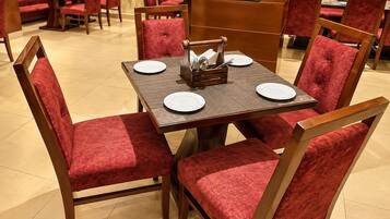 Comedor con una mesa cuadrada, cuatro sillas tapizadas rojas y un centro de mesa con platos y cubiertos.