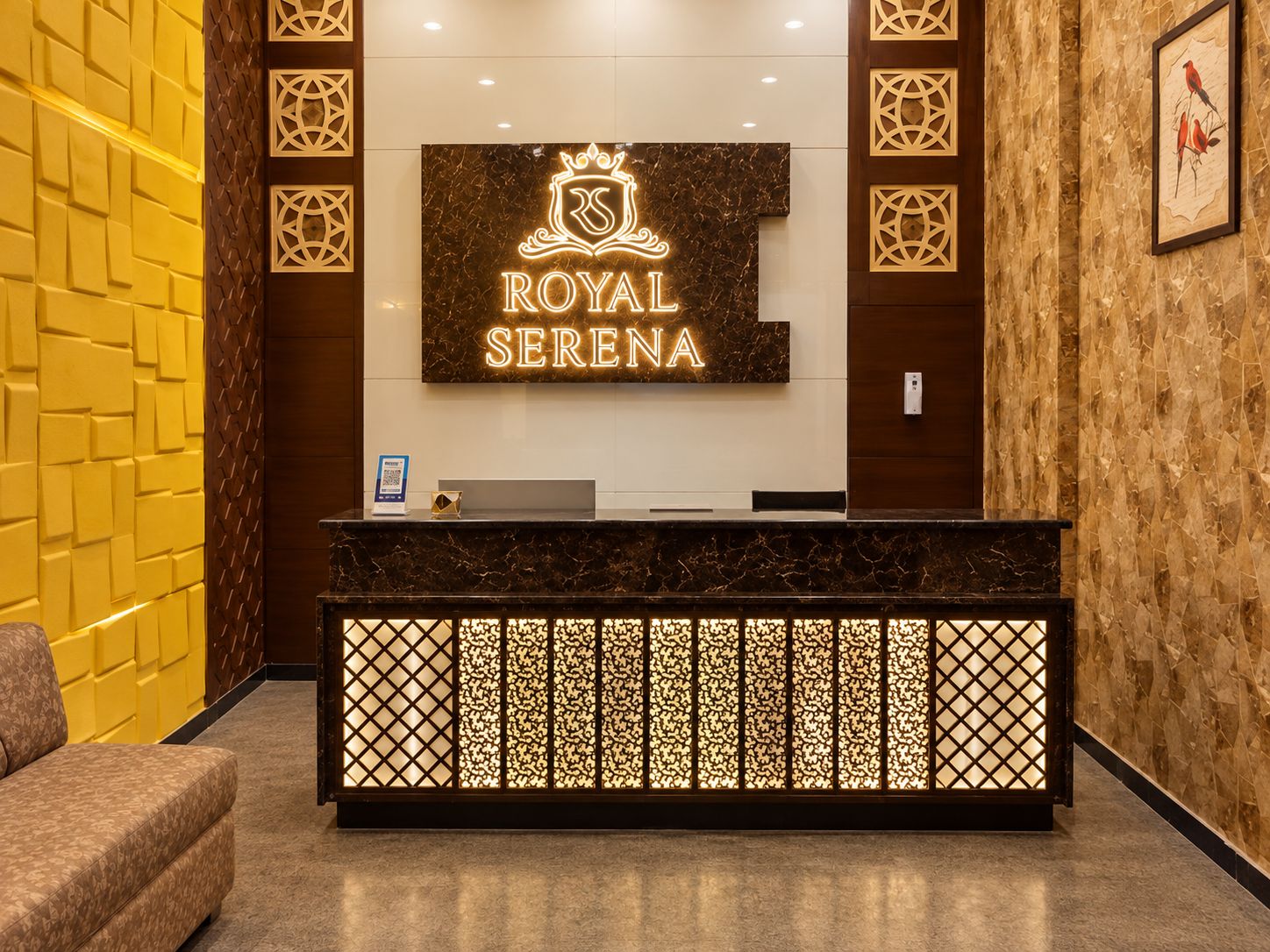 Una mesa de recepción con un cartel que dice 'ROYAL SERENA' y una obra de arte enmarcada con pájaros en la pared.