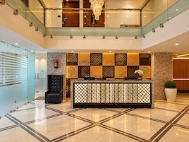 Vestíbulo de hotel con mostrador de recepción, candelabro, reloj y extintor.