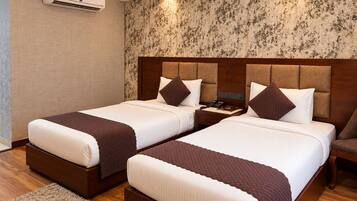 A hotel room with two beds, a wooden headboard, a wall-mounted air conditioner, and a patterned wallpaper.