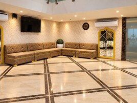 A hotel lobby with a sectional sofa, a flat-screen TV, a clock, and a decorative door with a crown emblem.