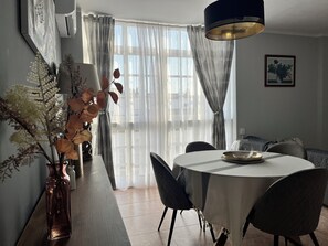 Un comedor con una mesa redonda, sillas, un florero con flores secas e iluminación colgante moderna.