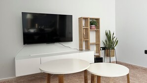 Una sala de estar moderna con un televisor de pantalla plana montado en una pared blanca, un aparador de madera con objetos decorativos y dos mesas redondas blancas.