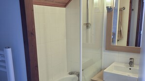 Un baño con cabina de ducha de vidrio, un lavamanos blanco y un mueble de tocador de madera.