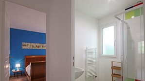 Ein Zimmer mit einem Bett, einem Nachttisch mit Lampe, einem Fenster, einer Dusche mit Glastür und einer farbenfrohen Kachelwand.
