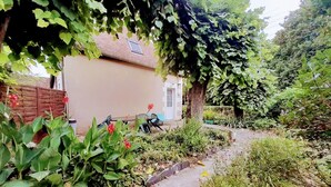 Ein Gartenweg führt zu einem Haus mit einem Ziegeldach, umgeben von üppigem Grün und blühenden Pflanzen.