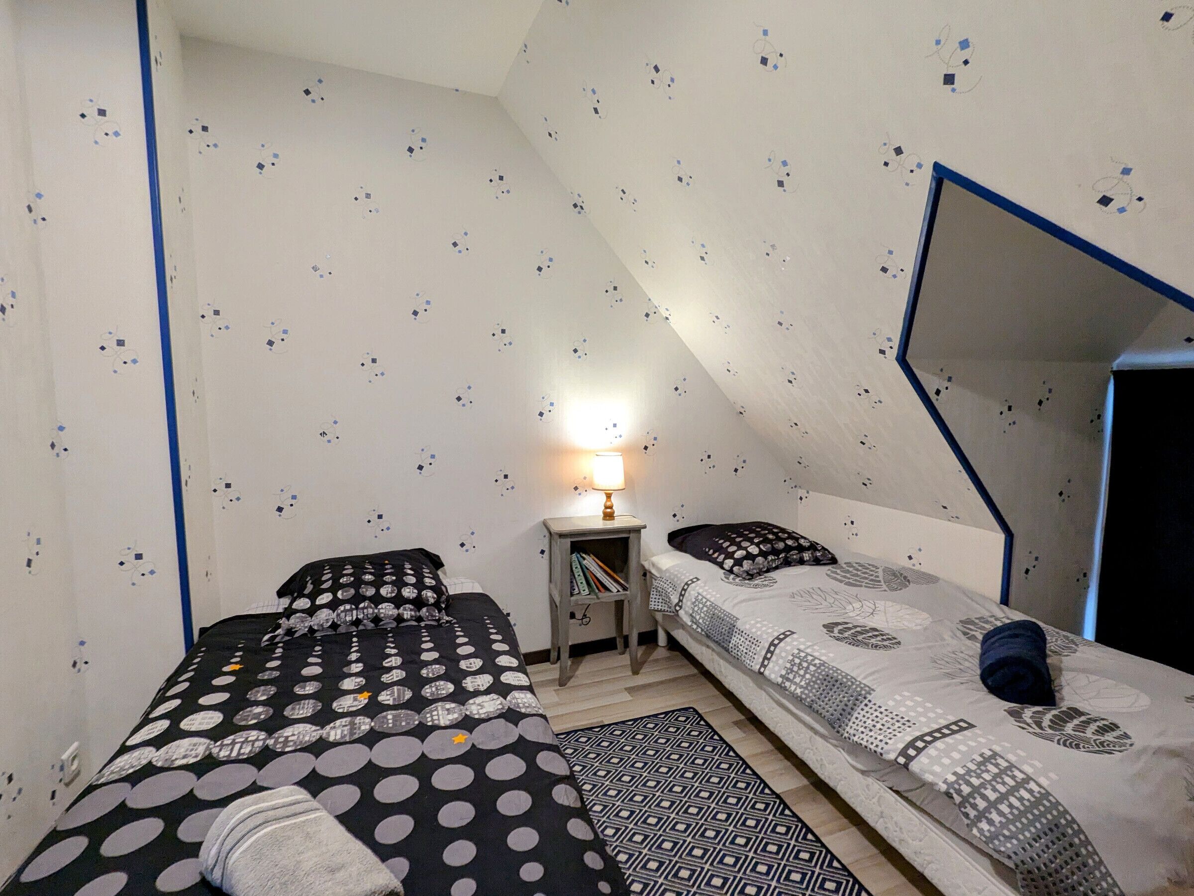 A small, compact room with two beds, a nightstand, and a lamp.